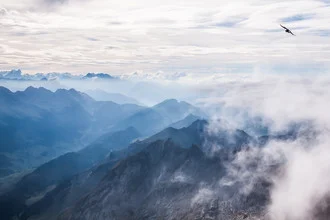 Photo art by Christian Görgen: Clouds above the Alps with a bird in flight.
