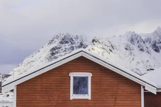 Rotes norwegisches Häuschen im Winter, umgeben von verschneiten Bergen.