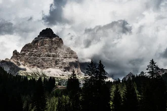 Photo of the Three Peaks in the Dolomites, surrounded by forests and mountains under a clear sky.