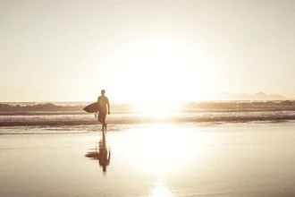Fotokunst: Surfer in der Dämmerung am Strand mit sanften Wellen des Ozeans.