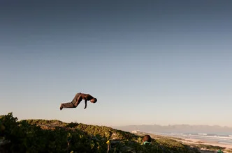 A boy joyfully leaps into the sky, surrounded by a vast blue sky.