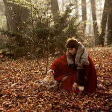 Photo art by Madelaine Grambow: Little Red Riding Hood in the woods with a bright red cape.
