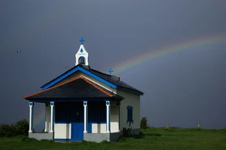 Photo art by Kolja Frohberger: rainbow over a picturesque chapel in nature