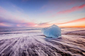 Ice block on a beach in Iceland, surrounded by sparkling water and gentle waves.