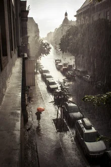 Straße in Neukölln mit Regenschirm im Regen, freundliche Stimmung.
