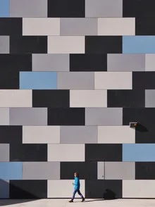 Photo art: people walking along a wall, captured in soft light tones.
