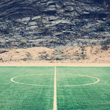 Fotokunst von Franz Sussbauer: Fußballspiel im Oman mit grünem Rasen und Felsen im Hintergrund