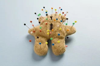 Voodoo-Puppe in ruhiger Komposition mit Stoffbär und Nadeln vor dunklem Hintergrund