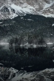 Foggy morning mood over Eibsee with gentle reflections of the mountains.