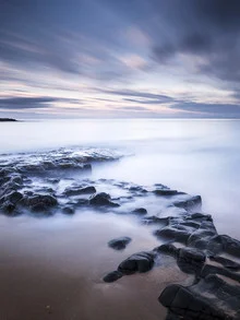 Photo art captures the rocky coast of Bamburgh at dusk with soft colors.