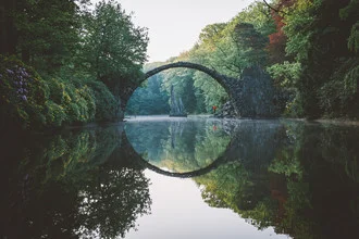 Wunderschöne Fotokunst von Johannes Hulsch: die Rakotzbrücke in einem Wald reflektiert im Wasser.