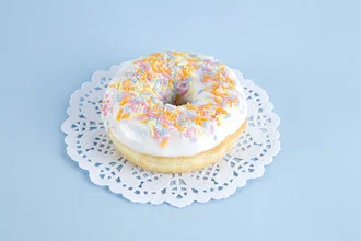 Photo art by Loulou von Glup: a vibrant donut on a delicate doily.