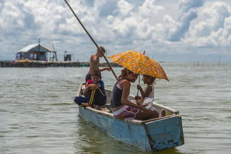 Children playing in a wooden boat under a colorful sun umbrella in Colombia.