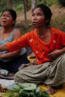 Frau raucht an einem Markt in Laos, umgeben von bunten Ständen und lebhaften Menschen.