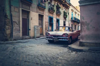Wandbild: Rosa Oldtimer auf den Pflastersteinen von Havanna, entspannte Stadtatmosphäre.