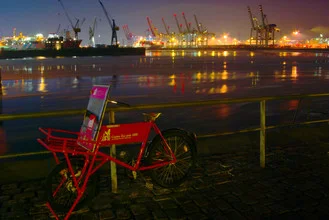 Night scene in Hamburg with an ice creation on a bicycle in front of cranes at the harbor.