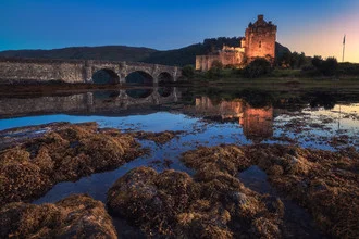 Sunset over Eilean Donan Castle in Scotland, soft colors in the sky.