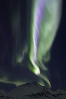 Colorful aurora over snow-covered mountains in Norway at night.