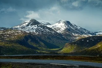 Moody photo art featuring clouds over Nordic mountains and a tranquil road.