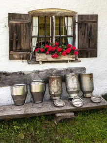 Milk cans on an alpine meadow in Bavaria, surrounded by flowers and a rustic bench.