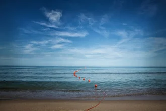 Fotokunst von Oona Kallanmaa: ruhige Küstenlandschaft mit sanften Wellen und blauen Himmel.