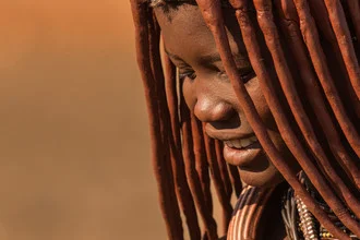 Fotografie einer Himba-Frau in Namibia mit orangefarbenem Tuch und braunen Akzenten