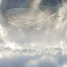 Frozen soap bubble in sunlight, delicate and cool, adorned with sparkling ice crystals.