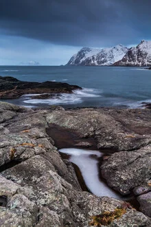Landscape image of the Lofoten in Norway featuring rocks and cold waters.