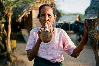 Frau mit Kokusnuss und Zigarre in Myanmar, entspannte Alltagsatmosphäre.