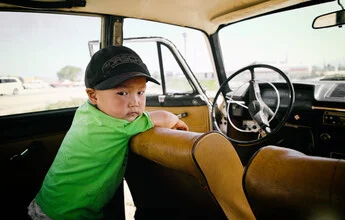 Boy in an old Lada in Kyrgyzstan, happily sitting in the car.