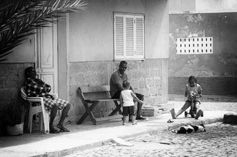 Photo art by Jochen Fischer: lively street scene in Cape Verde featuring family and dog.