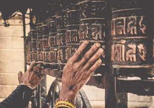 Hands turning prayer rolls in a Buddhist temple in Nepal.