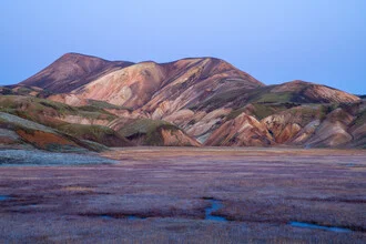 Colorful mountains of Iceland under a clear blue sky with soft clouds.