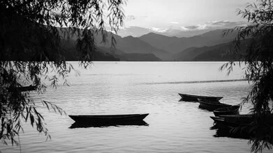 Calm water in Nepal with a rowboat in front of majestic mountains