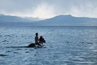Fotokunst: Junge reitet auf einem Pferd im Wasser in Kirgisistan.