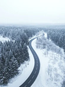 Schneebedeckte Straße durch den Wald, sanfte Kurven im Winterlicht.