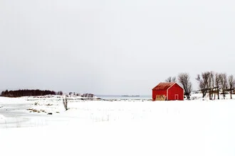 Winter landscape featuring a red cabin by the fjord, surrounded by snow-covered mountains.
