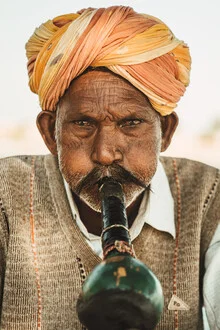 Indian flutist playing in the desert under a clear blue sky.