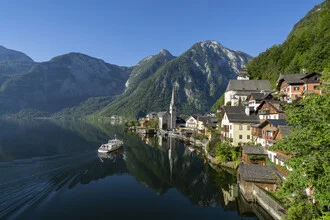 Charming photo art of Hallstatt featuring a clear blue sky and a boat on the lake.