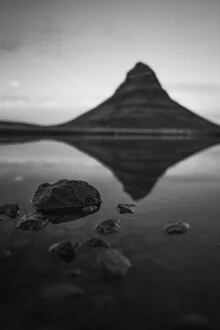 Calm reflection on water, surrounded by stones and a majestic mountain landscape.