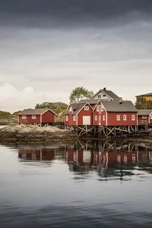 Fisherman's cottages in Norway, painted red, surrounded by calm water and gentle mountains.