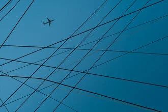 Photo art by AJ Schokora: airplane flying over wires and blue sky.