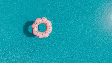 Photo of a colorful donut floating in a pool, surrounded by clear water.