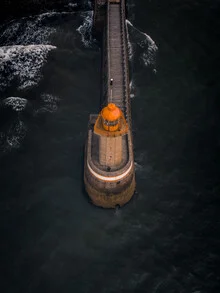 Aerial view of the lighthouse in Fécamp by the coast, waves wash over the rocks.