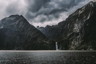 Fjord landscape in New Zealand featuring dramatic clouds and a waterfall